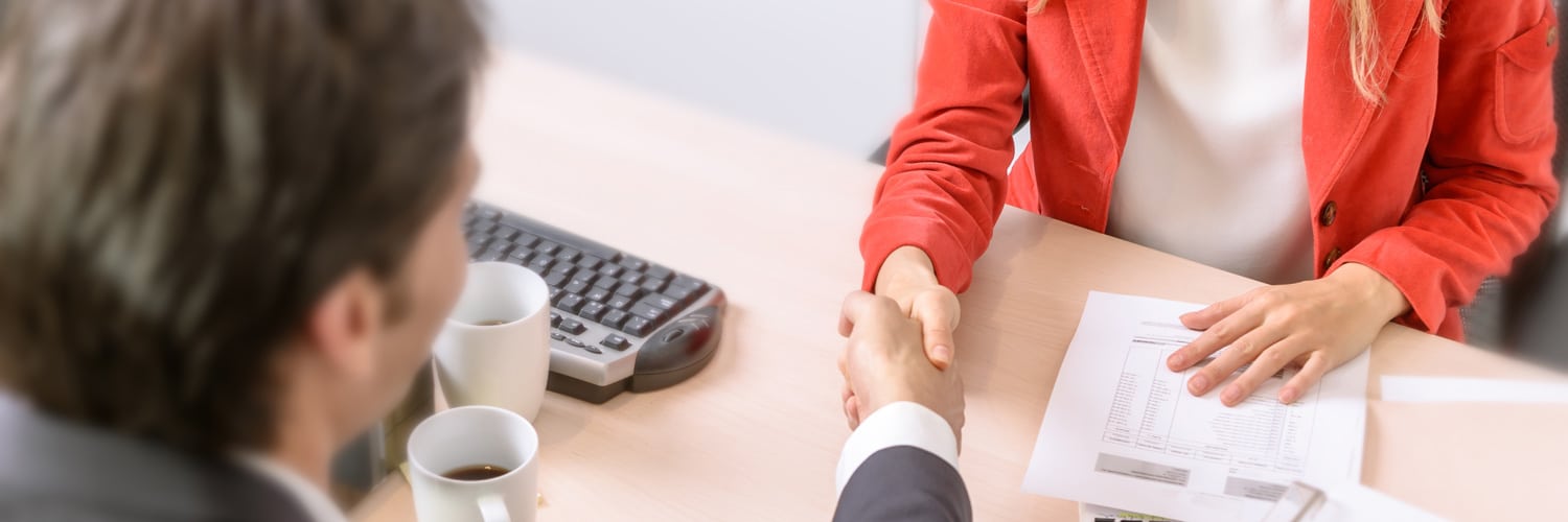 Close up shot of a man and a woman shaking hands at a job interview.